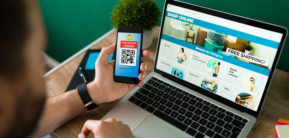 young-man-using-discount-coupon-his-smartphone-some-online-shopping-laptop